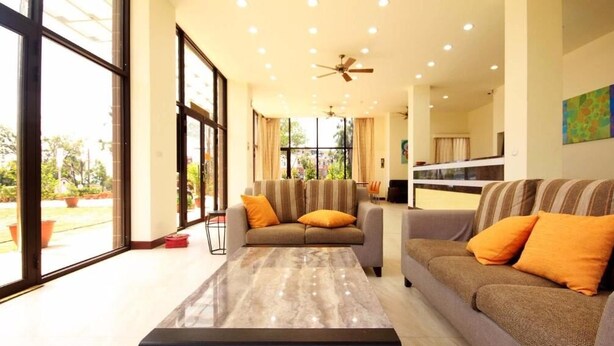 A spacious living room with large windows, a ceiling fan, and a sofa with orange cushions. - Line In B&B (Jinhu)