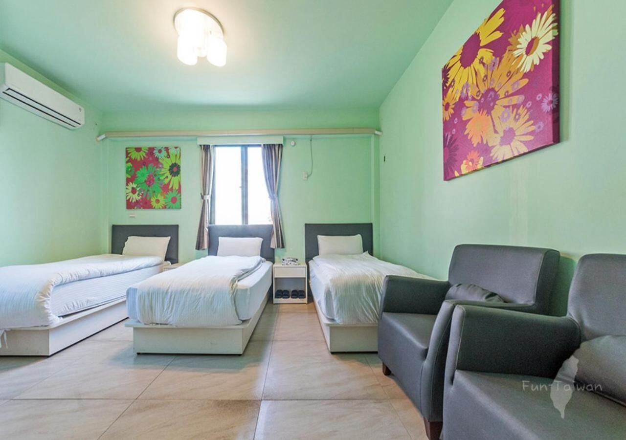 A hotel room with two single beds, a sofa, a small table, and a window with curtains.