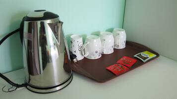 Una tetera eléctrica de acero inoxidable, seis tazas con estampado floral y dos sobres de té sobre una bandeja marrón.