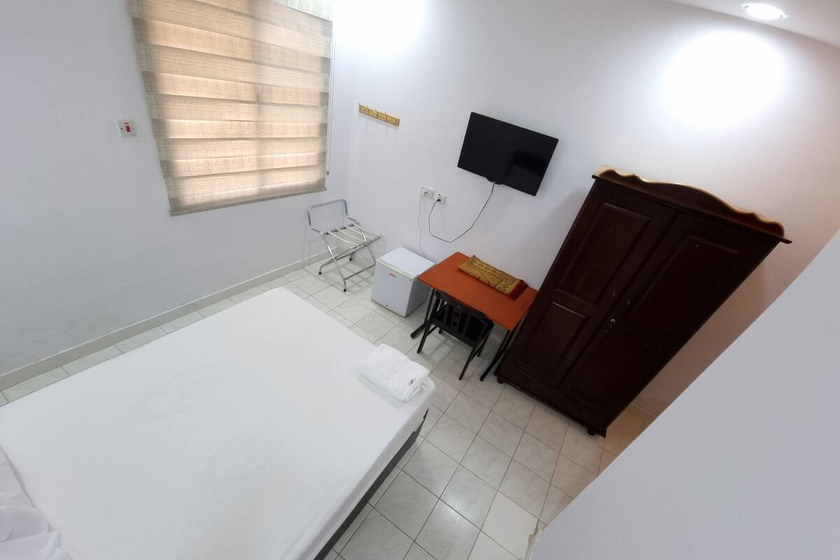 A small, clean room with a bed, a desk, a chair, a TV, and a wardrobe.