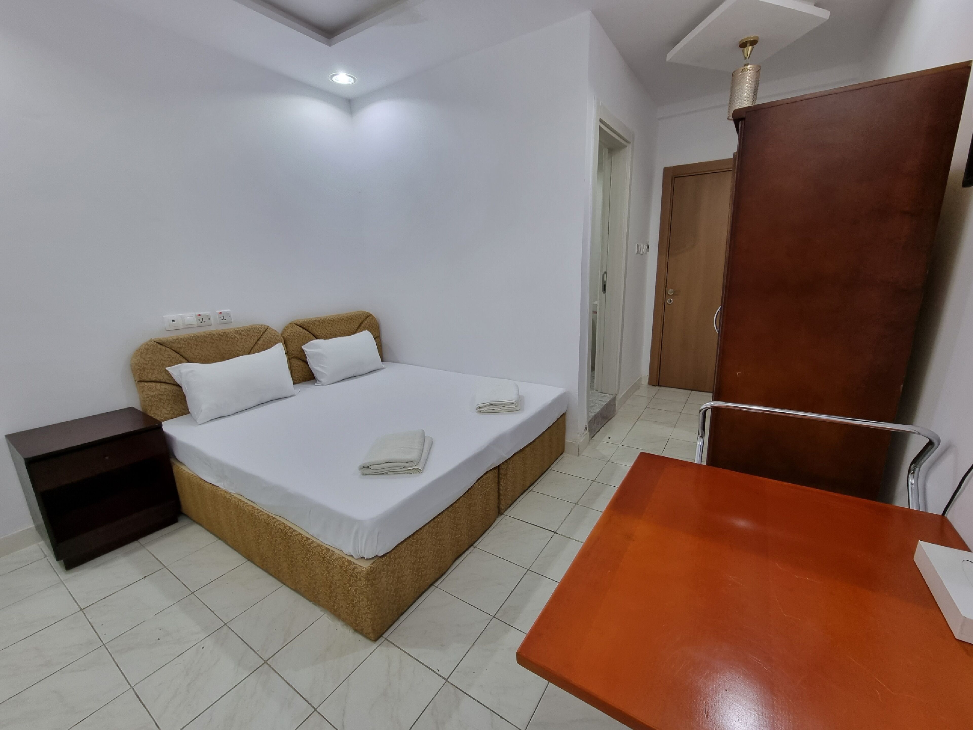 A bedroom with a bed, a nightstand, a wooden wardrobe, and a small table.