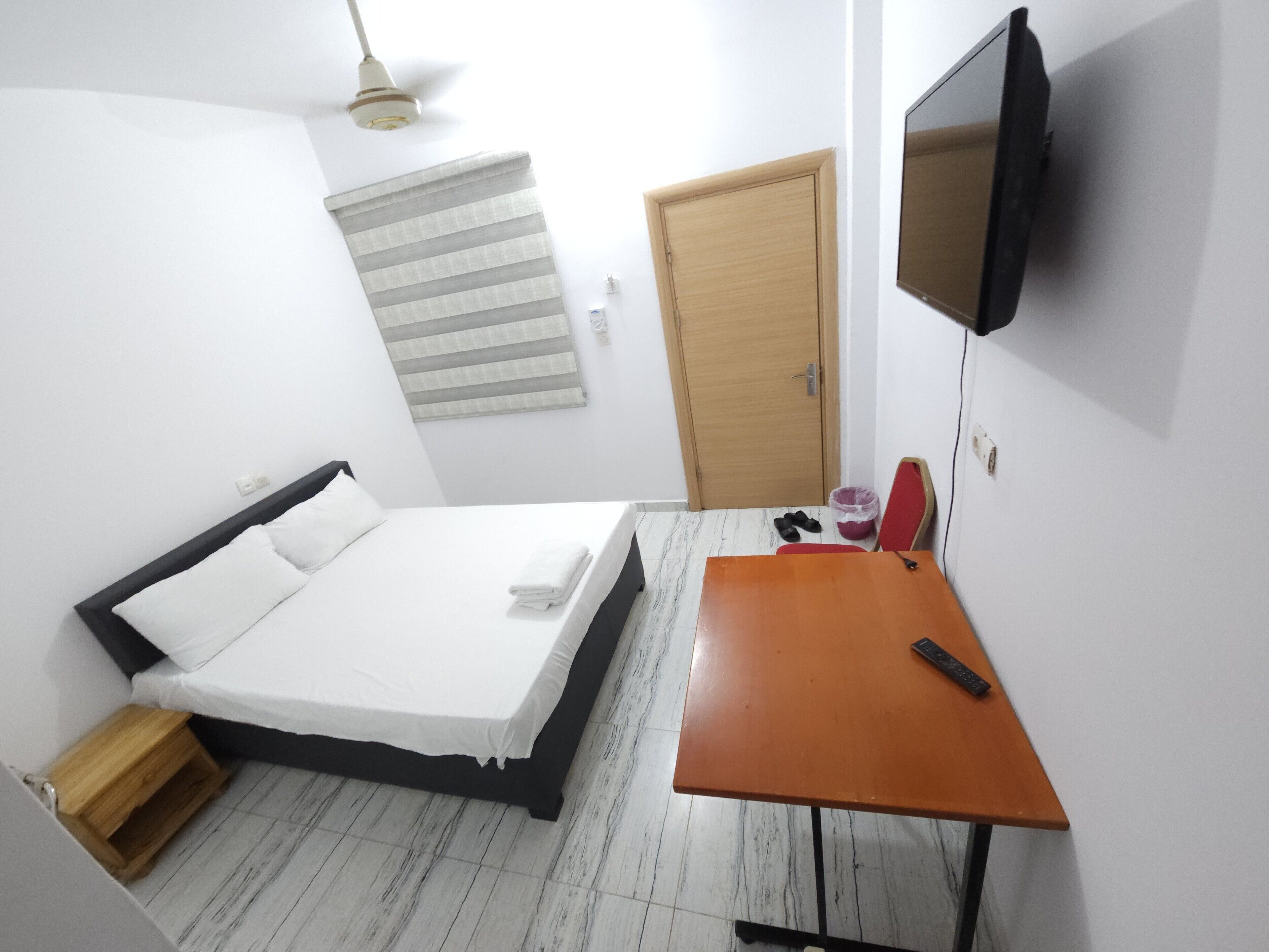 Un dormitorio con una cama, un escritorio, un televisor y una puerta.