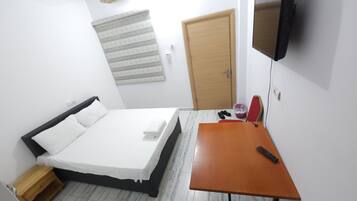 Un dormitorio con una cama, un escritorio, un televisor y una puerta.