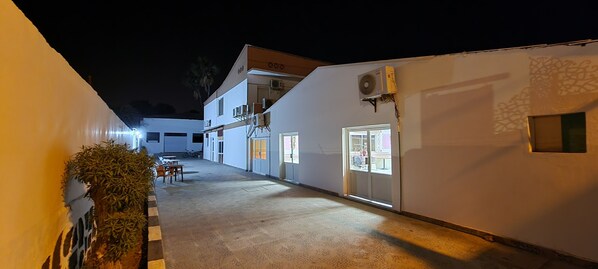 A narrow corridor with a tiled floor, a white wall with a window, and an air conditioning unit mounted on the wall.