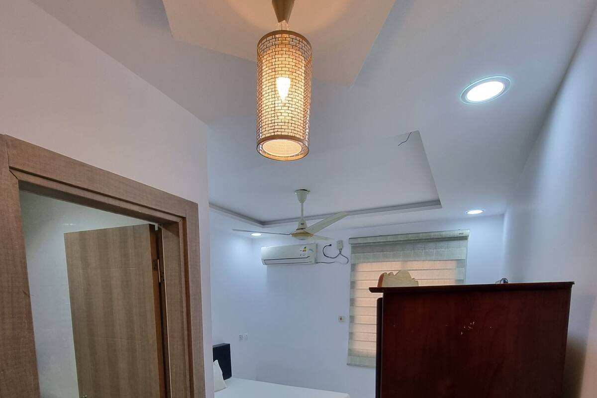 A bedroom with a bed, a ceiling fan, an air conditioning unit, and a wooden wardrobe.