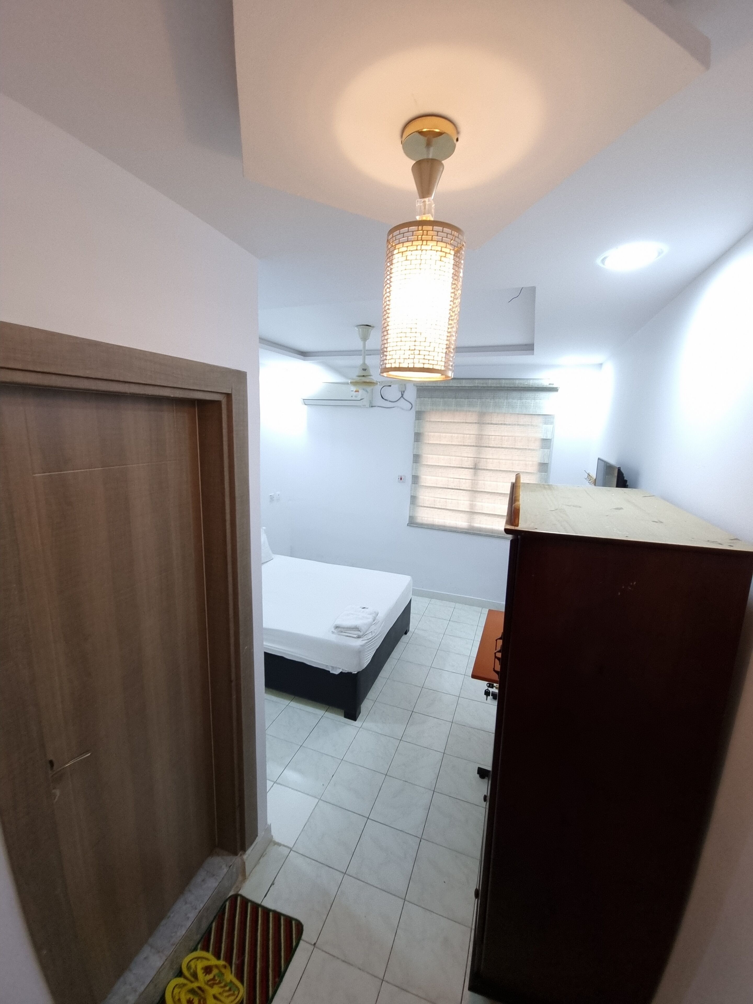 Una habitación de hotel compacta con cama, un pequeño escritorio, una lámpara de techo y una ventana con persianas.