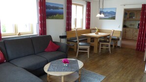 A cozy living room with a sofa, a round coffee table with a vase, a dining table with chairs, and a kitchen area with wooden cabinets. - Spacious, inviting apartment near Füssen  close Neuschwanstein castle (Hopferau)
