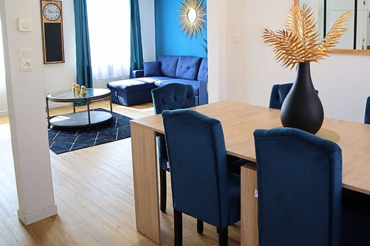 Un salon moderne avec un canapé bleu, une table à manger et des chaises, ainsi qu’un vase décoratif.