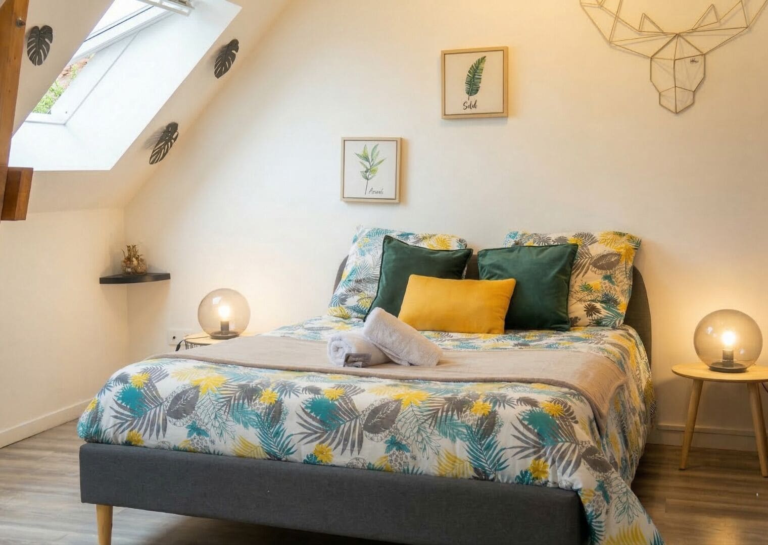 Une chambre à coucher avec un lit, des oreillers, une table de chevet, une œuvre d’art murale et une lucarne.