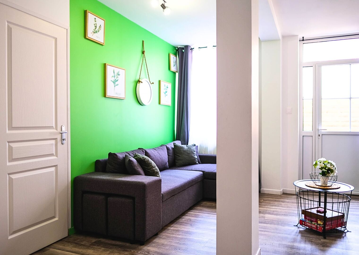 A room with a green wall, a grey sofa, and a small round table with a plant.
