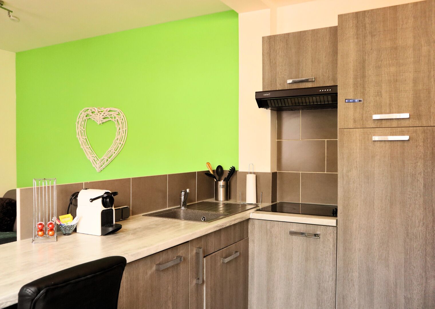 A modern kitchen with a green accent wall, a heart-shaped decoration, and a built-in stove.