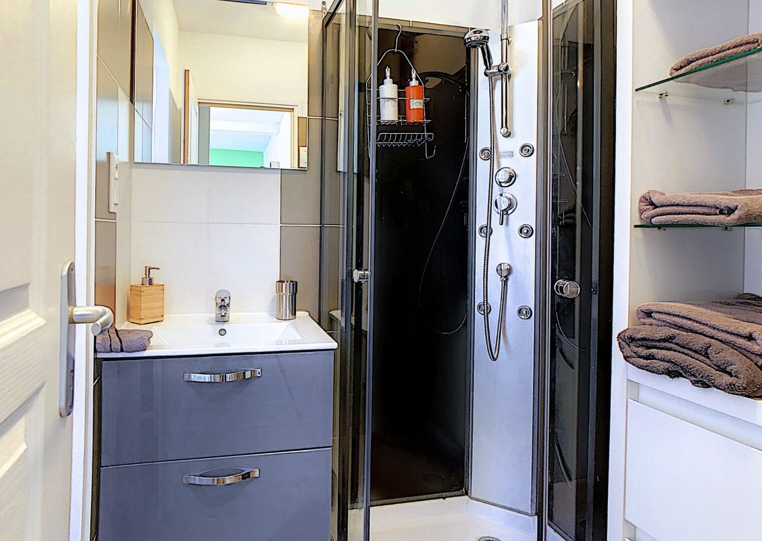 A modern bathroom with a glass shower enclosure, a sink with a soap dispenser, and a towel rack.