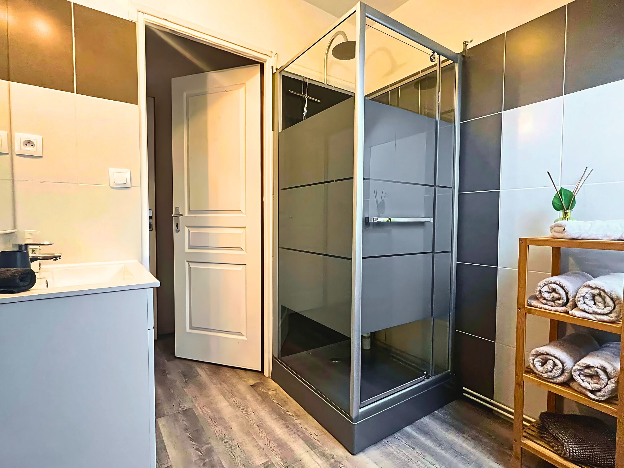 Une salle de bain moderne avec une douche à parois de verre, un lavabo blanc et une étagère où sont posées des serviettes.