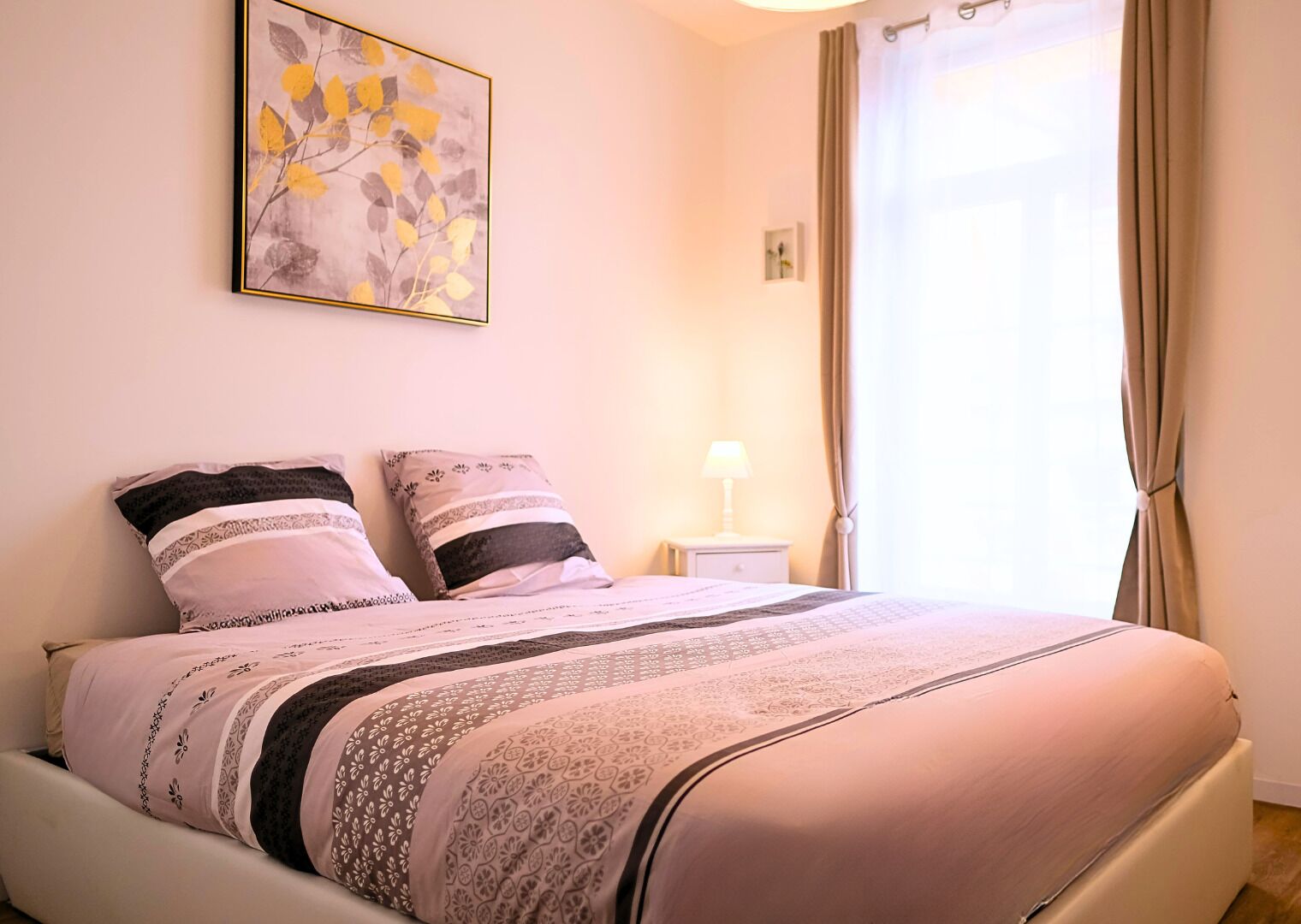 A neatly made bed with patterned bedding, a bedside lamp, and a framed artwork on the wall.