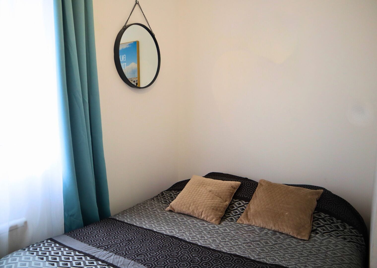 A bed with patterned bedding, two pillows, and a hanging mirror.
