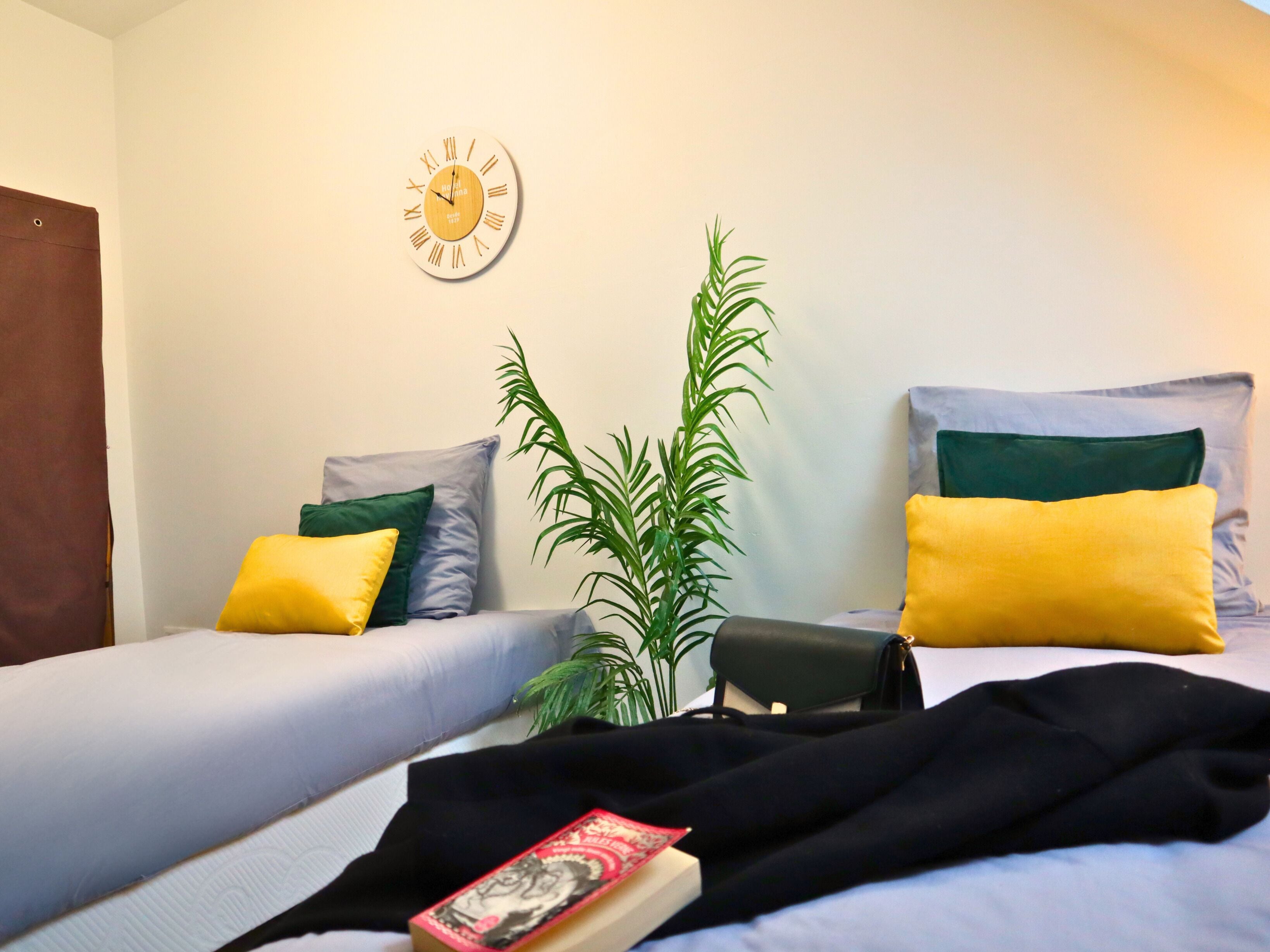 Een kamer met twee bedden, een wandklok en een kamerplant.