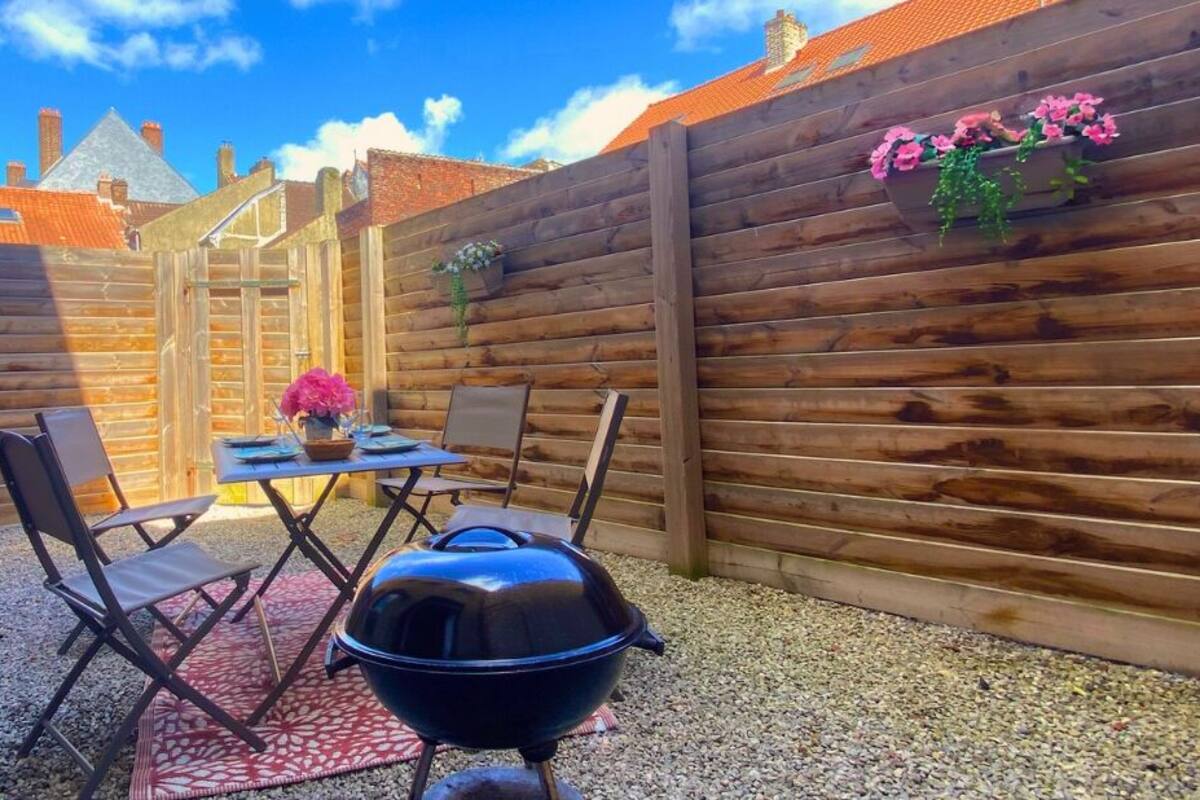 Un jardin avec une clôture en bois, un barbecue et une table avec des chaises.