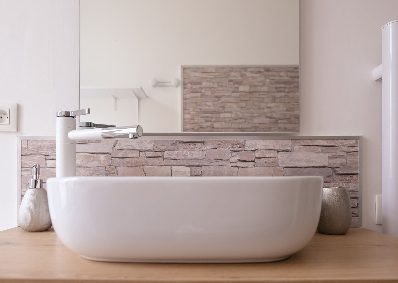 A modern bathroom with a large vessel sink, a stone backsplash, and a mirror above it.