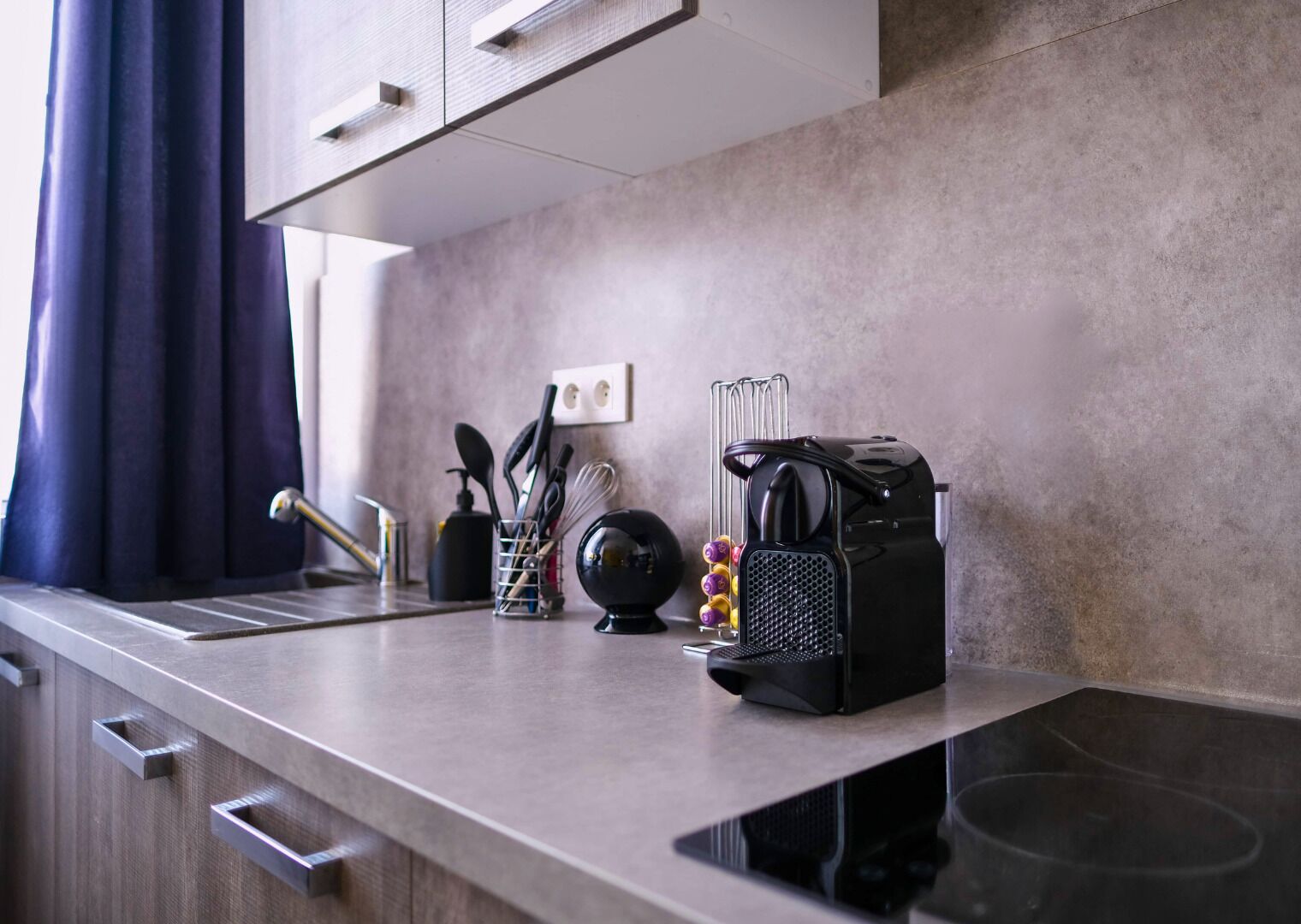 A modern kitchen with a stainless steel countertop, a coffee machine, and kitchen utensils.