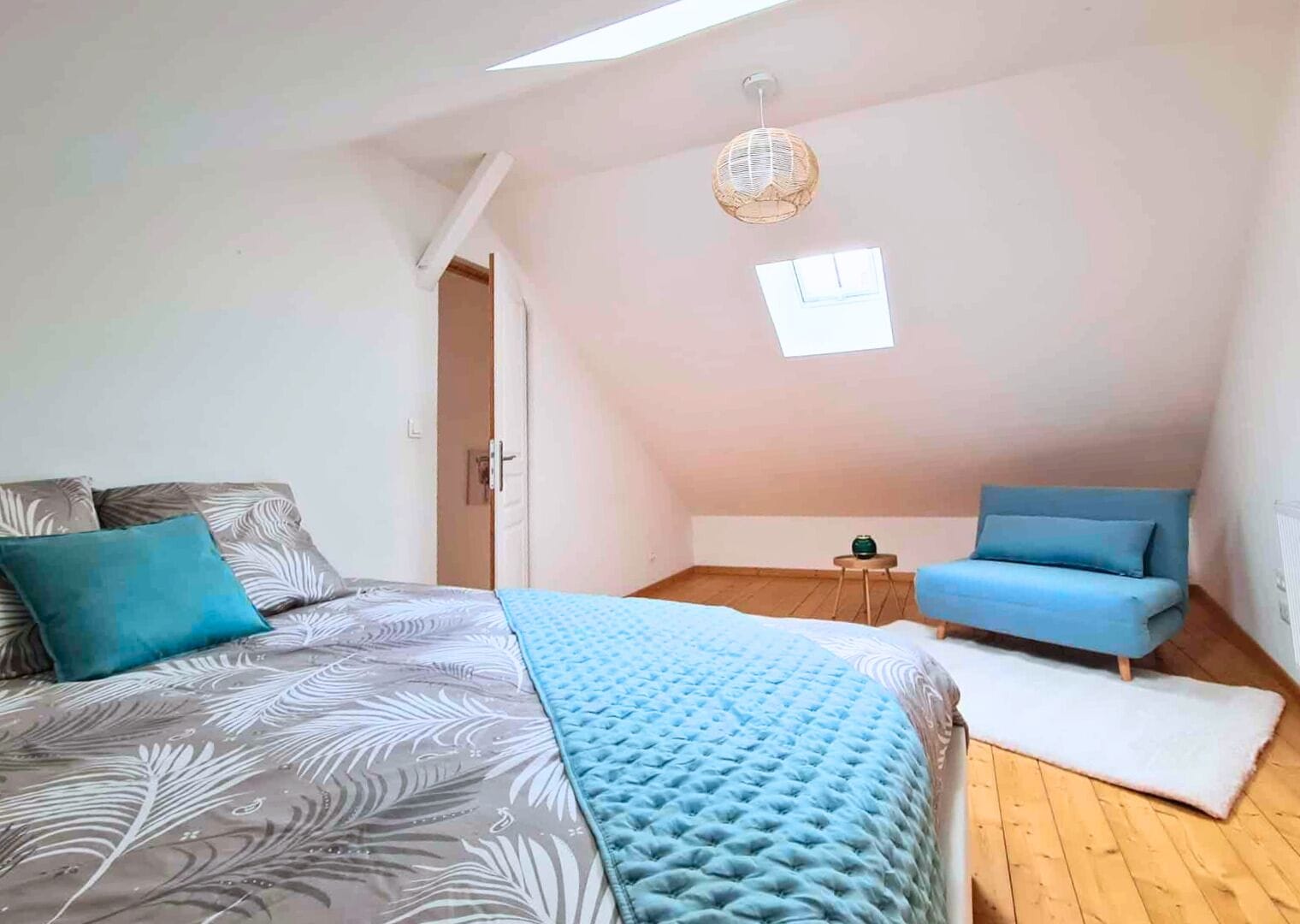 A bedroom with a bed, a blue sofa, a small table, and a window.