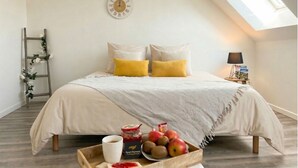 Un dormitorio con cama, almohadas, un reloj, una escalera, una lámpara, una bandeja con comida y una ventana.