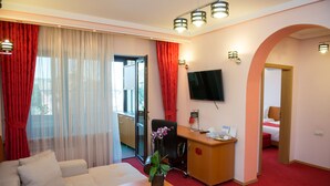 A hotel room with a sofa, a desk with a computer, a TV, and a red carpeted floor. - Pensiunea President (Deva)