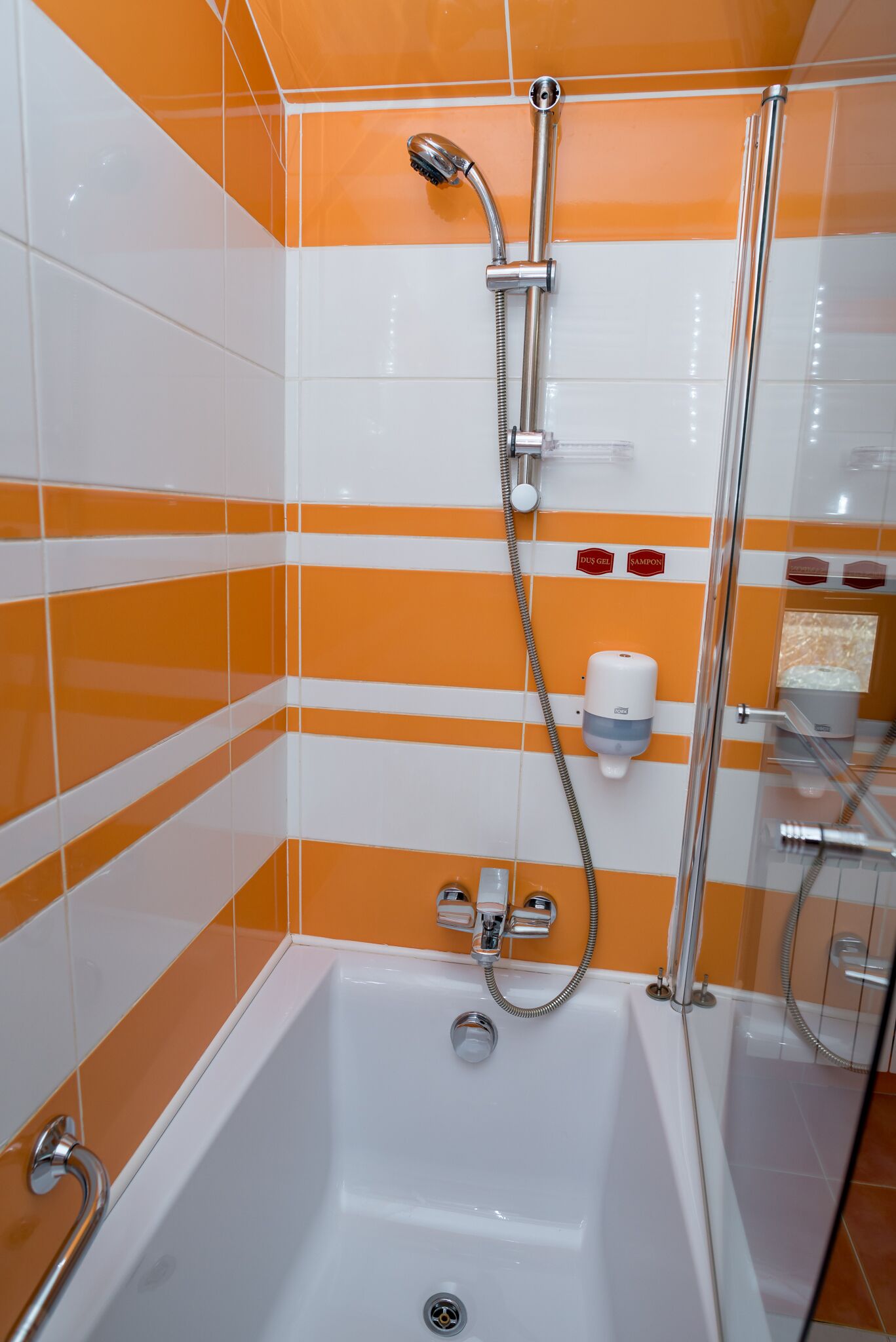 Un baño con una bañera blanca, una cabina de ducha de cristal y paredes con azulejos blancos y anaranjados.