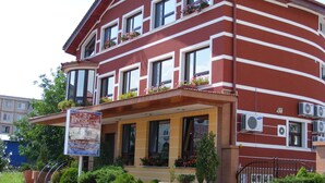A red and white striped building with multiple windows, some with flower boxes. There is a signboard in front with text. - Pensiunea President (Deva)