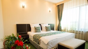 A hotel room with a large bed, a bench, a nightstand, and a bedside table with a vase of flowers. - Pensiunea President (Deva)