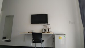 Une chambre d’hôtel équipée d’un téléviseur à écran plat fixé au mur, d’un petit bureau avec une chaise, d’une bouilloire et d’un réfrigérateur.