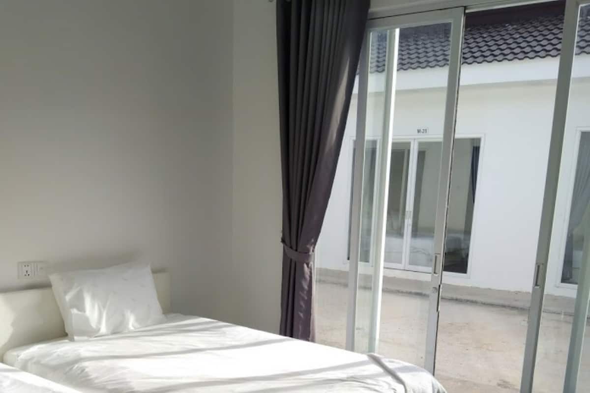 A hotel room with a bed, a chair, and a view of the outside through a glass door.