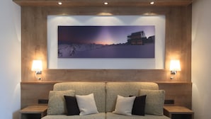 A modern living room with a two-seater sofa, two wall-mounted lamps, and a large framed picture of a mountain landscape. - Garbershof (Soelden)