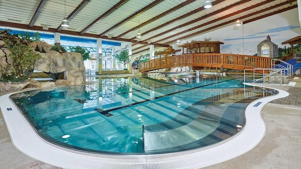 An indoor swimming pool with a wooden bridge, a mural, and a rocky landscape backdrop. - Garbershof (Soelden)