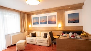 A hotel room with a sofa, a dining table with breakfast items, and three framed pictures on the wall. - Garbershof (Soelden)