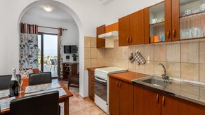 A kitchen with wooden cabinets, a stove, and a sink. There is a dining area with a table and chairs. - Beautiful apartment in Kostrena (Kostrena)