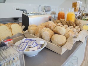 A breakfast buffet with various breads, rolls, and a bowl of butter packets. - Penedo da Saudade Suites & Hostel (Coimbra)