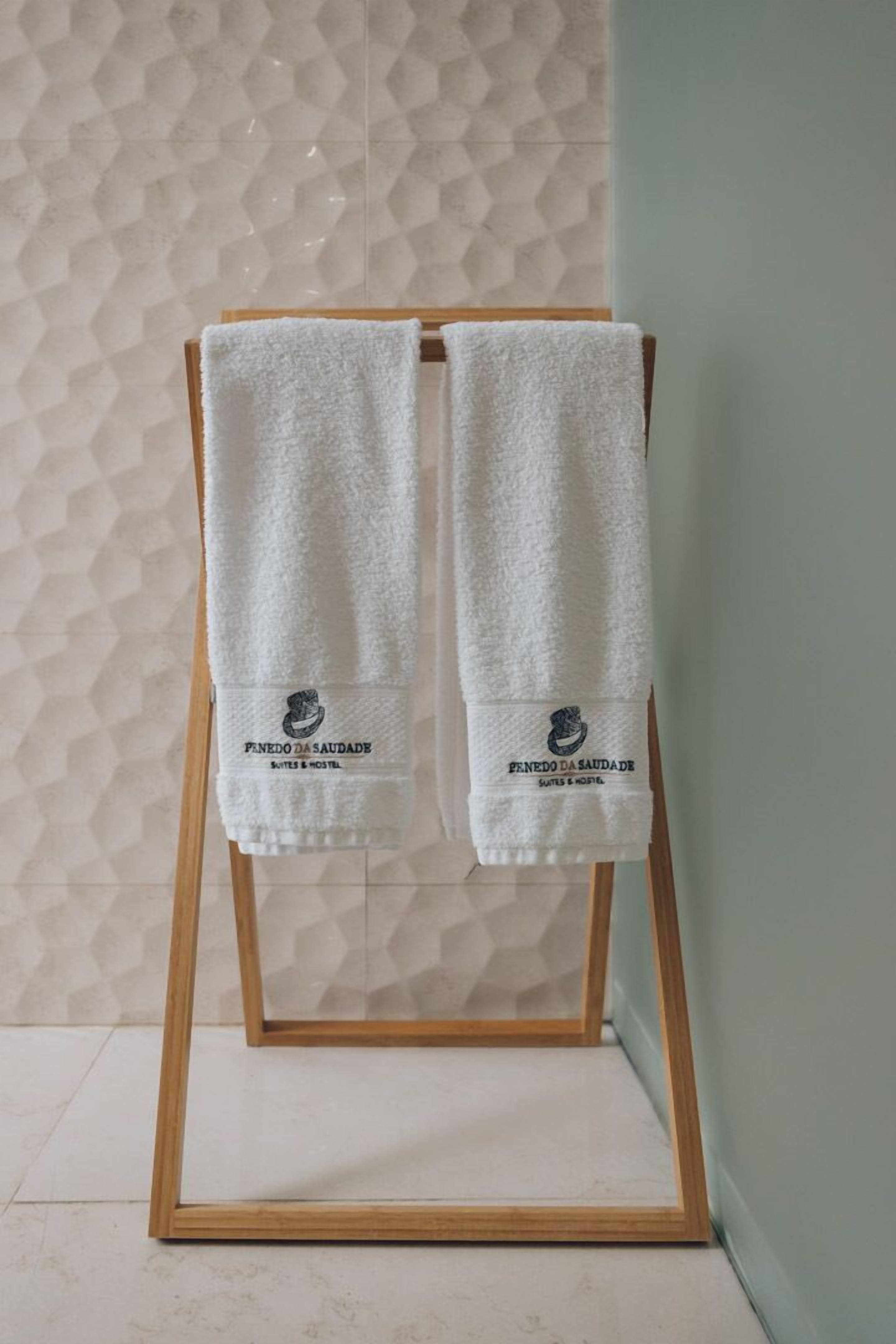 Dos toallas blancas colgadas en un toallero de madera con un logotipo y texto que indican que provienen de un hotel.