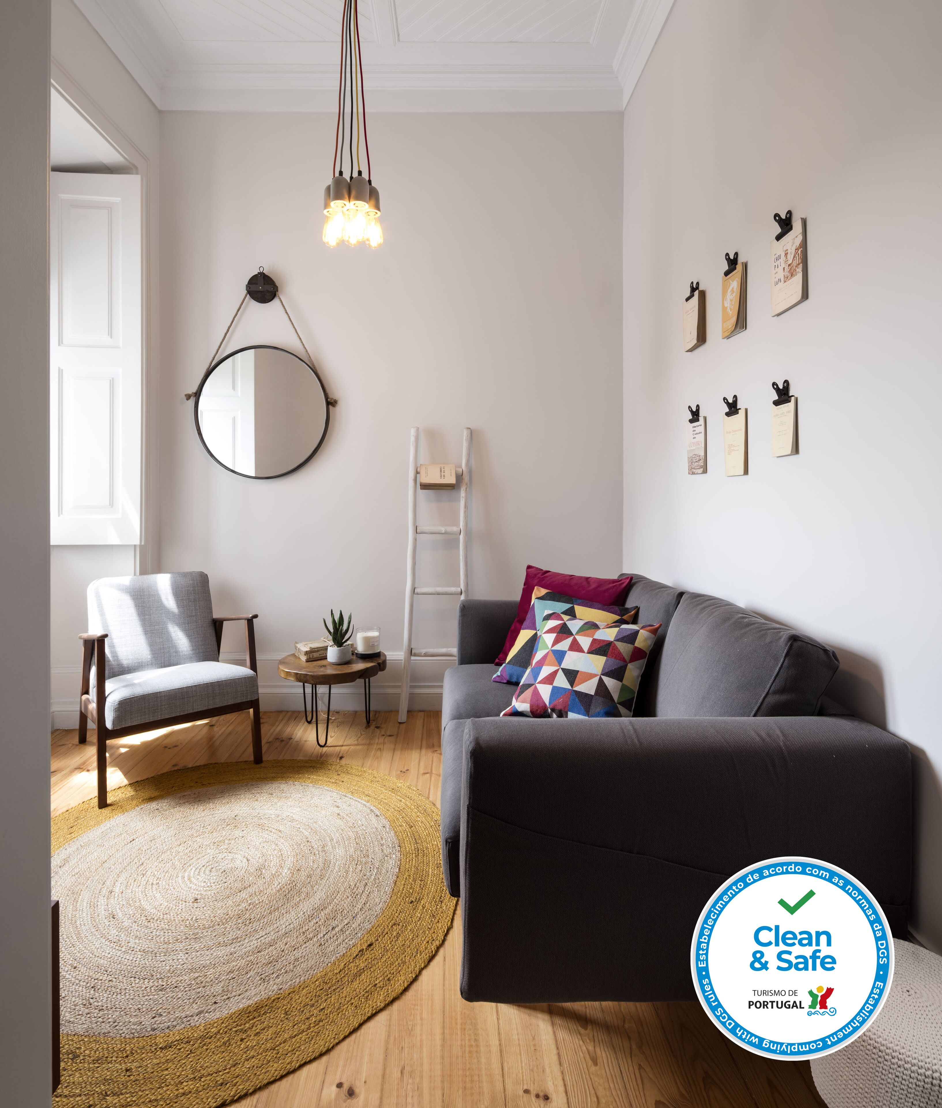 Una sala moderna con un sofá gris, un espejo redondo y una lámpara colgante.