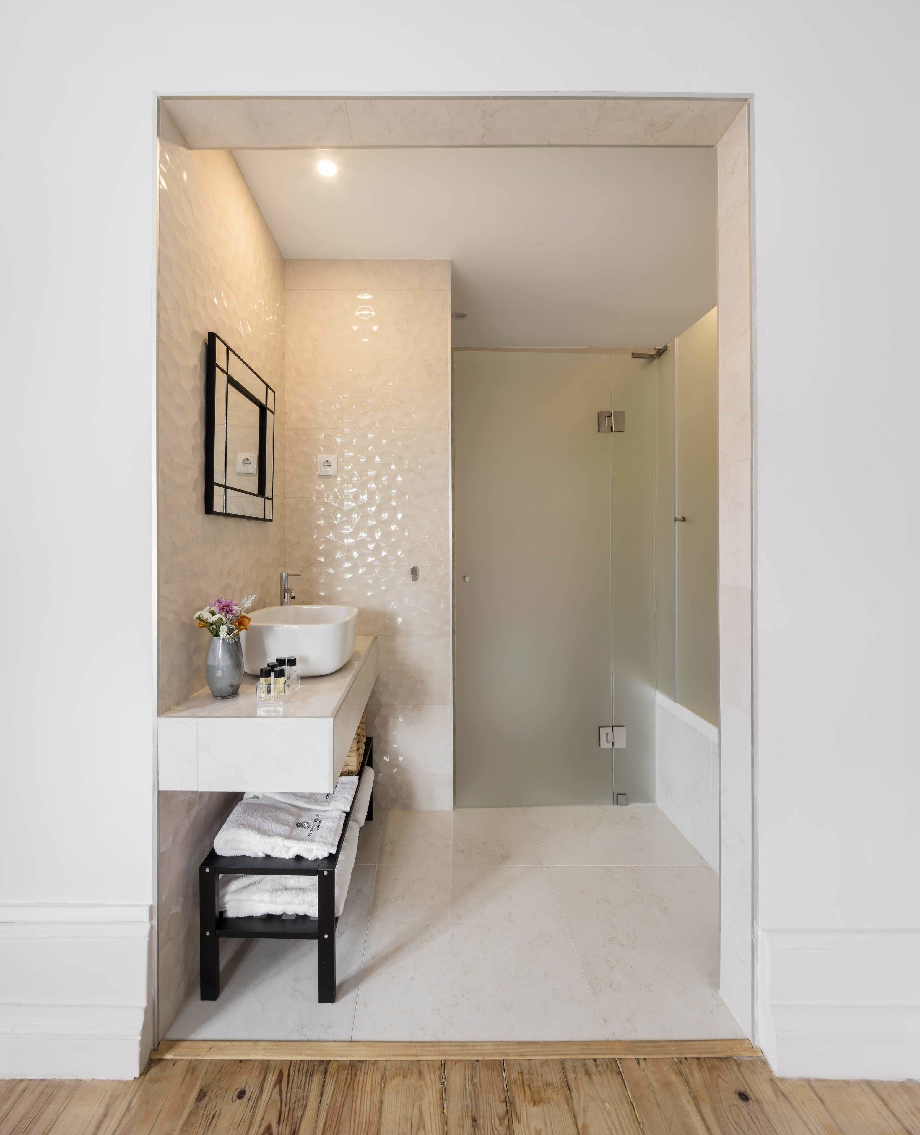 A modern bathroom with a white vanity, a glass shower enclosure, and a wooden bench.