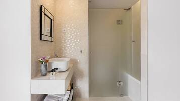 A modern bathroom with a white vanity, a glass shower enclosure, and a wooden bench.