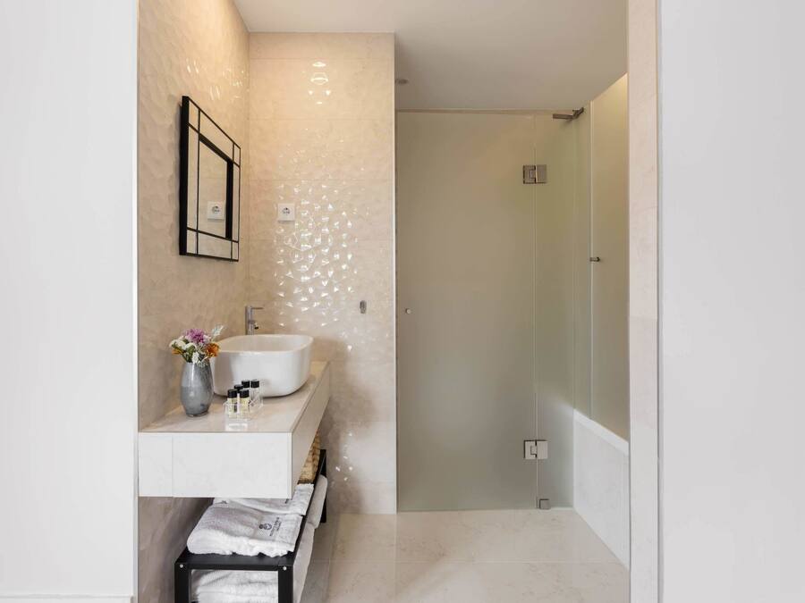 A modern bathroom with a white vanity, a glass shower enclosure, and a wooden bench.