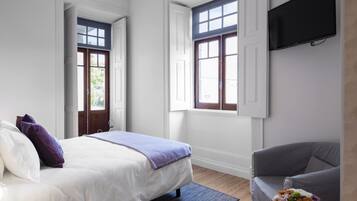 Un dormitorio moderno con una cama, un sillón gris, una mesita con flores y un televisor instalado en la pared.