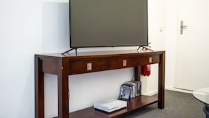 A wooden console table with a flat-screen TV mounted above it, a fire extinguisher on the wall, and a few video games on the lower shelf. - Bed'n'Work Apartment Prenzlauer Berg (Berlin)