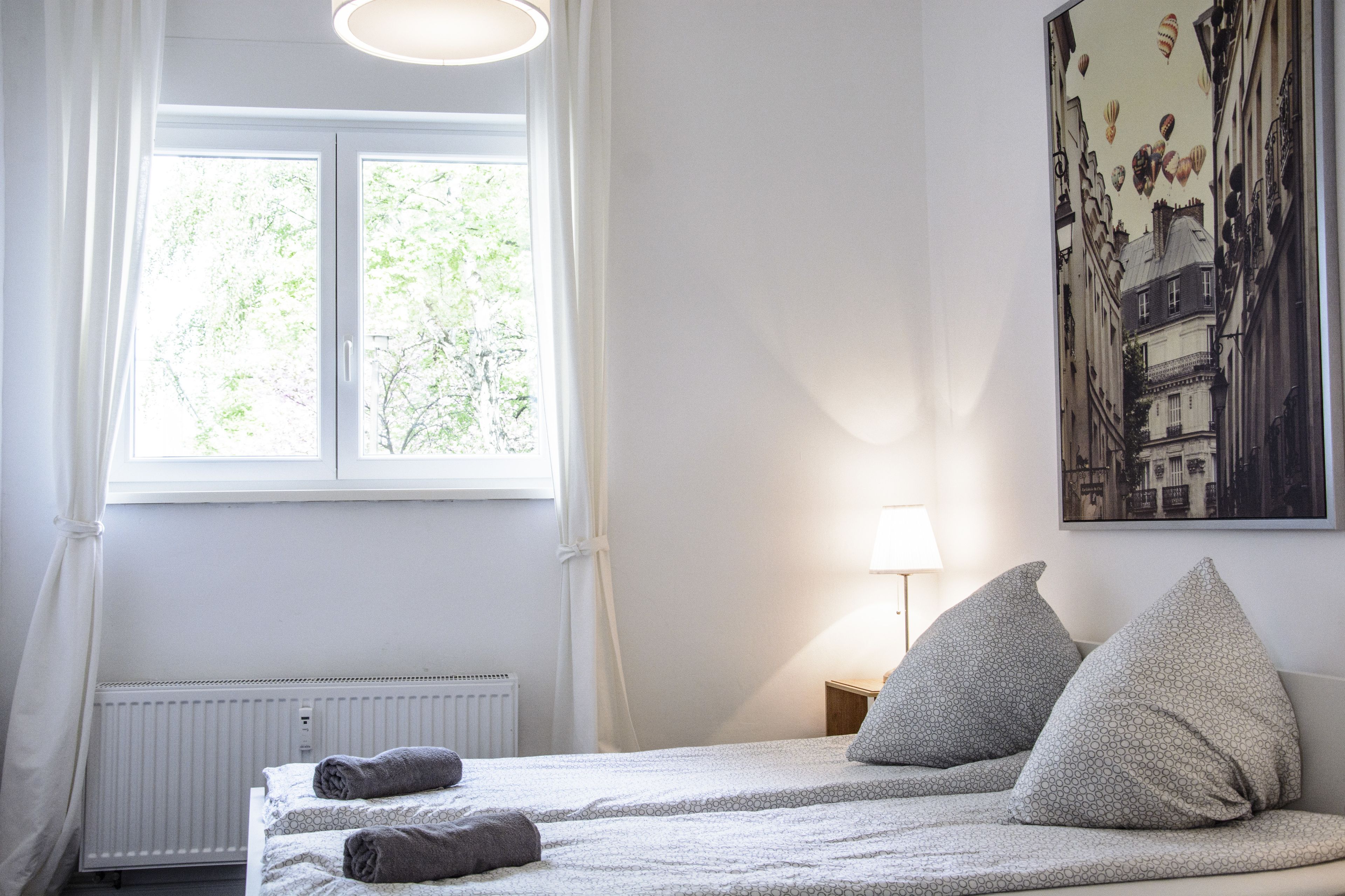 A bedroom with a bed, a window, a radiator, and a painting on the wall.