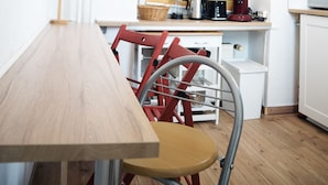 A small kitchen with a wooden table, a red chair, a window with blinds, and a microwave on the counter. - Bed'n'Work Apartment Mitte (Berlin)