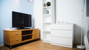 A room with a wooden entertainment center, a white shelving unit, and a floor lamp. - Bed'n'Work Apartment Mitte (Berlin)
