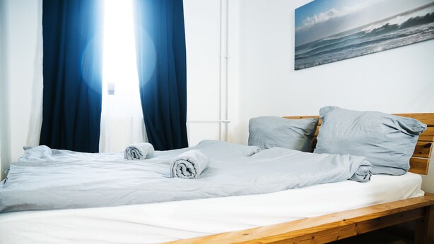 A single bed with a wooden frame, grey bedding, and two pillows. - Bed'n'Work Apartment Mitte (Berlin)