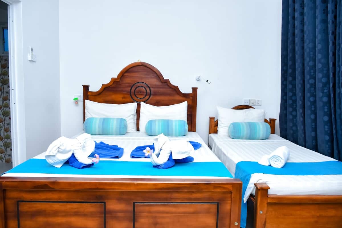Une chambre d’hôtel avec deux lits, chacun doté d’une tête de lit en bois, de couvre-lits bleus et d’oreillers blancs. Un rideau bleu est accroché sur le côté droit.