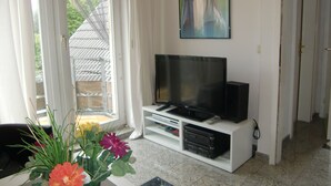 Un soggiorno con televisione su un mobile bianco, un quadro appeso al muro e una porta che dà su un balcone.