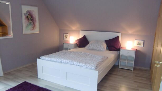 Una camera da letto con un letto bianco, un tappeto viola e due comodini con lampade.